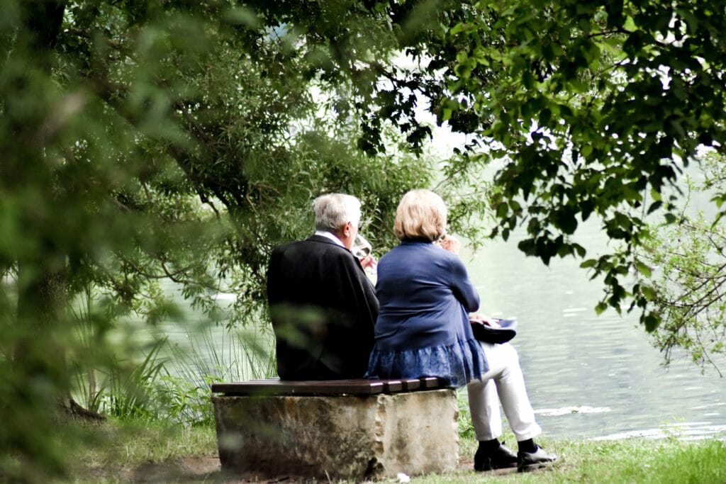 backside of an elderly couple drinking wine while looking at a lake