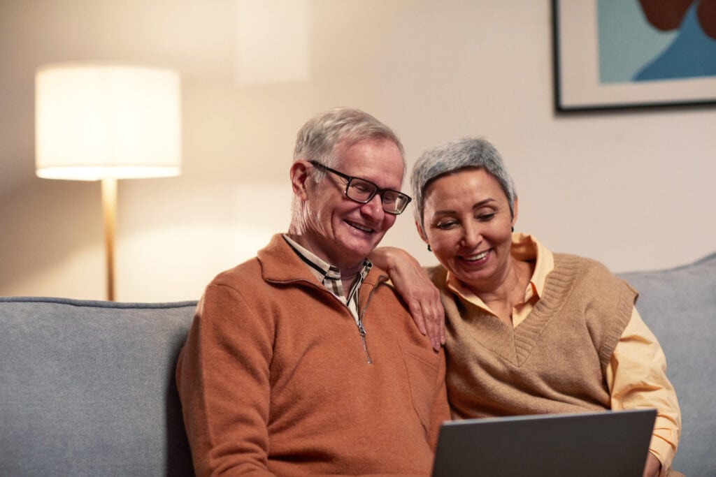 elderly couple sitting on a couch looking at a laptop