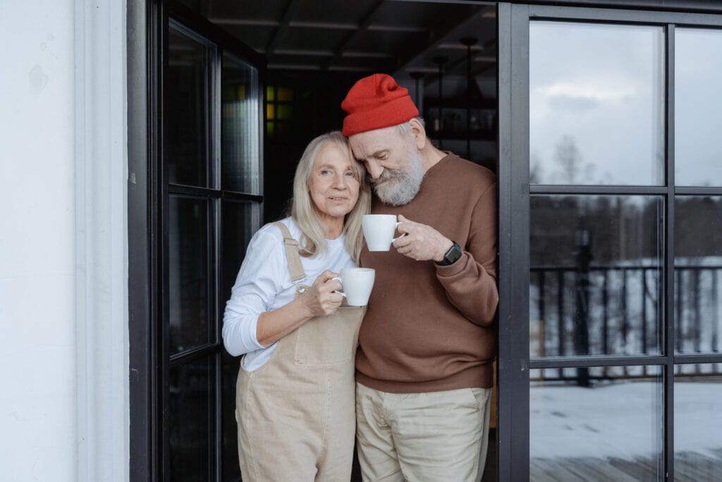 older man and woman standing in front doorway drinking coffee